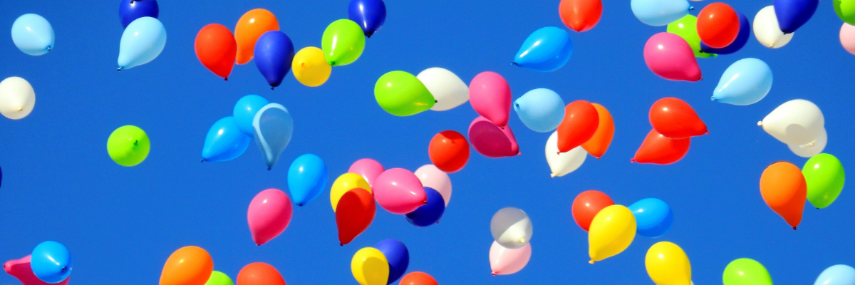 Dozens of colourful balloons flying in a blue sky
