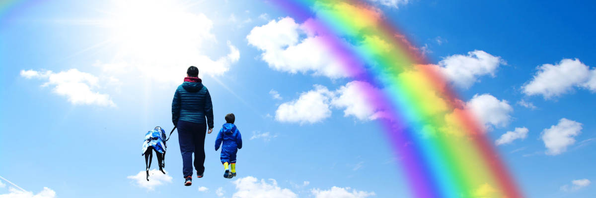 Woman, child and dog walking toward a rainbow with blue sky background