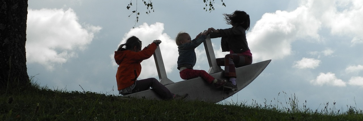 Three small children on a seesaw at dusk
