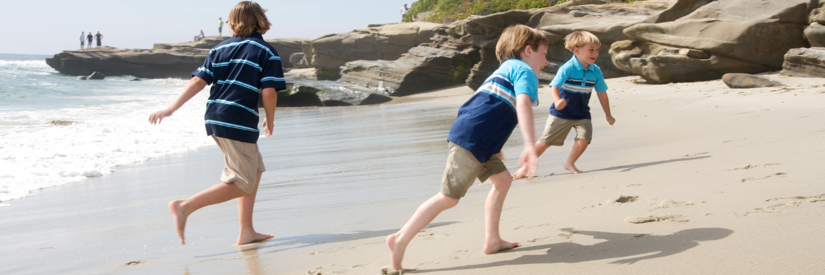 Three young brothers running around on the beach