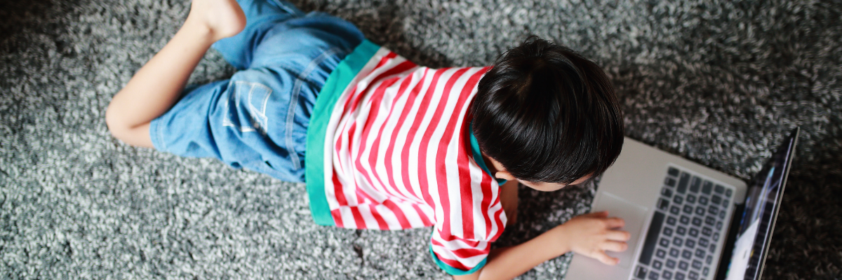 A small boys lies on the floor looking at a laptop