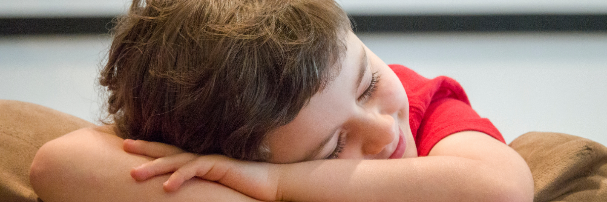 A boys smiles whilst resting his head on his arms