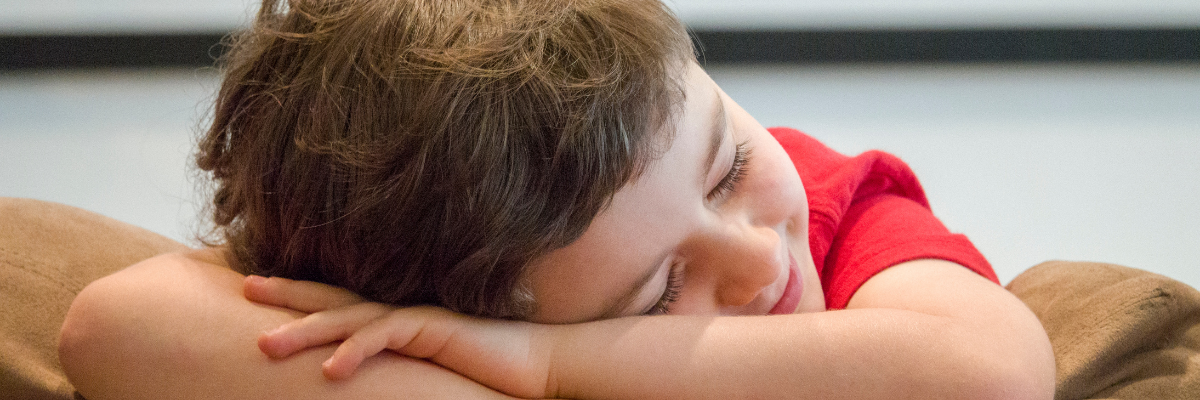 A boys smiles whilst resting his head on his arms 