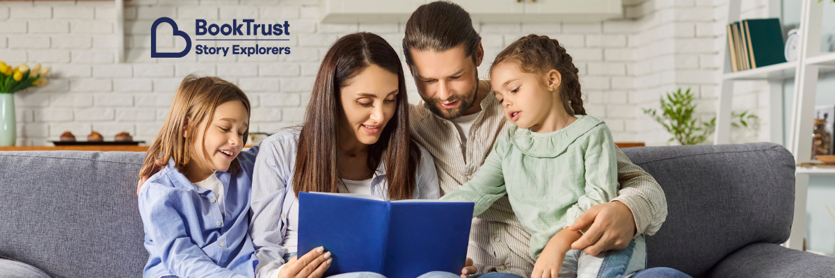 Mum, dad, and two young daughters reading a book together on a sofa